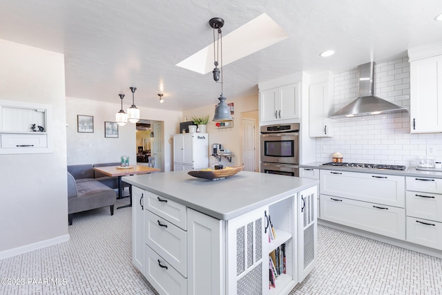 kitchen with white cabinets, hanging light fixtures, wall chimney exhaust hood, appliances with stainless steel finishes, and a kitchen island