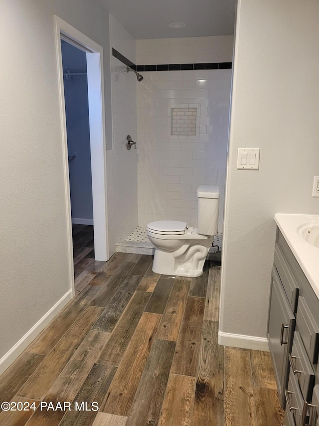 bathroom featuring a tile shower, vanity, hardwood / wood-style flooring, and toilet