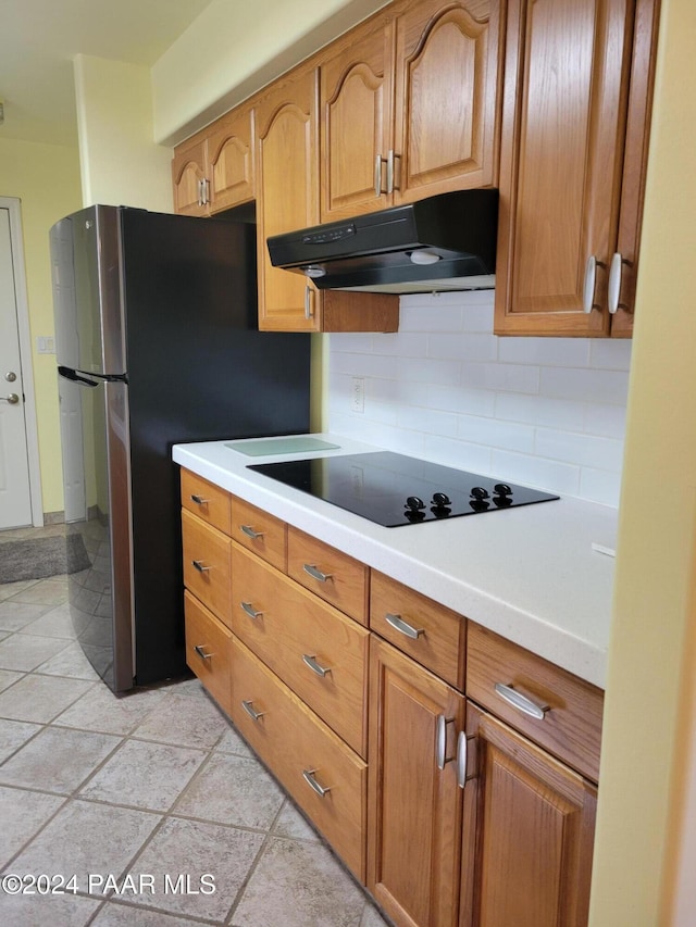 kitchen featuring decorative backsplash, black electric stovetop, and light tile patterned floors