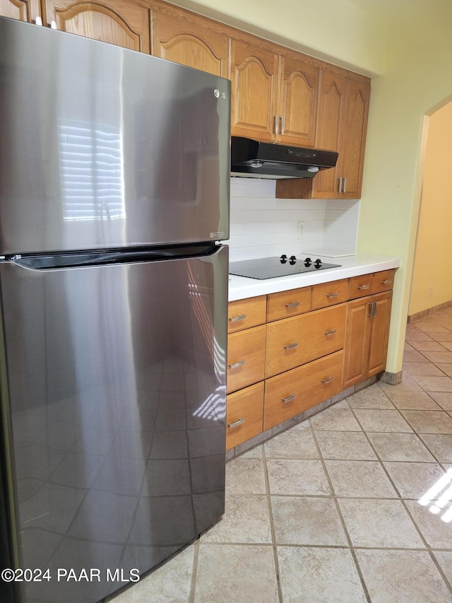 kitchen featuring black electric stovetop, decorative backsplash, and stainless steel refrigerator