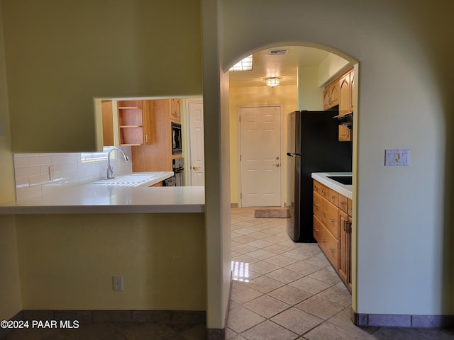 kitchen featuring sink, backsplash, kitchen peninsula, light tile patterned floors, and black appliances