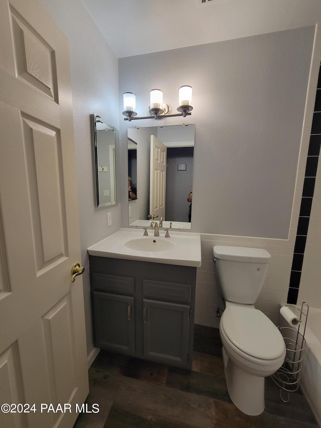 bathroom with toilet, vanity, tile walls, and hardwood / wood-style flooring