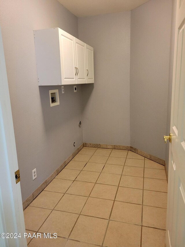 clothes washing area with hookup for an electric dryer, hookup for a washing machine, light tile patterned floors, and cabinets