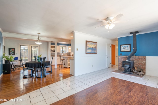 tiled living room featuring crown molding, a wood stove, and a ceiling fan