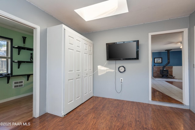 unfurnished bedroom with a closet, a skylight, a wood stove, and wood finished floors