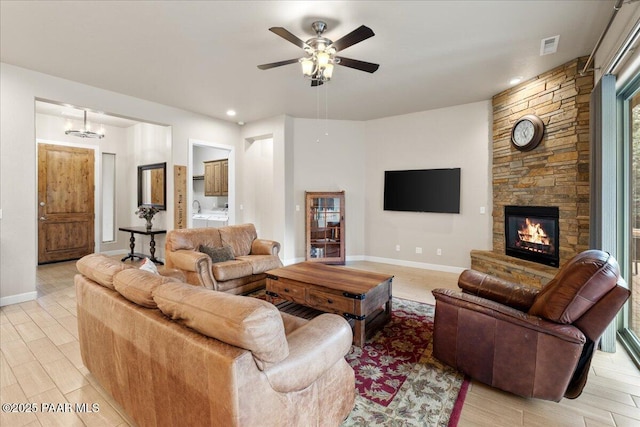 living area featuring visible vents, baseboards, a stone fireplace, ceiling fan, and light wood-type flooring