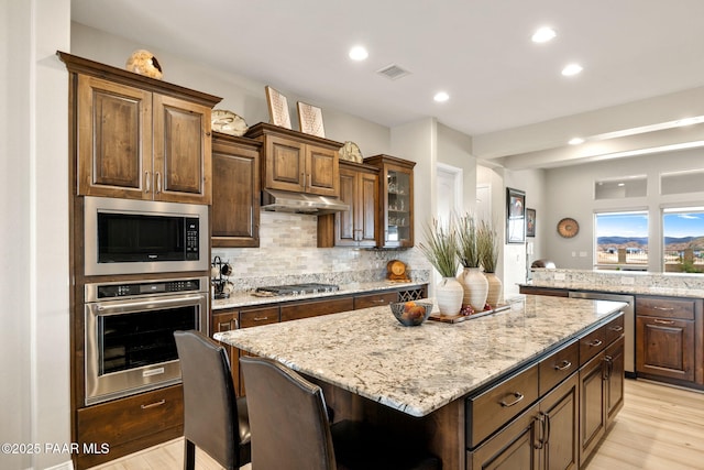 5242 High Cliff Way, Prescott, AZ 86301 - kitchen featuring stainless steel appliances, under cabinet range hood, decorative backsplash, light wood-style floors, and a center island