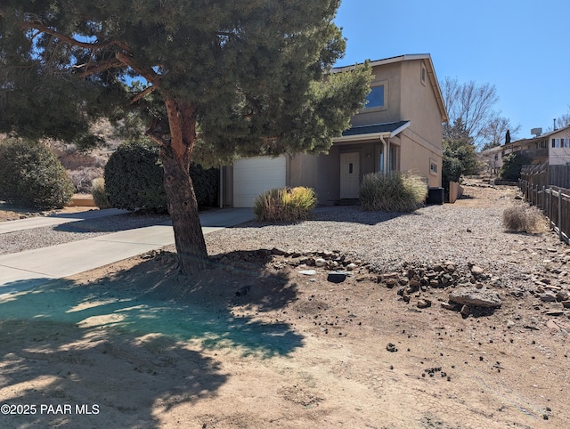 view of property hidden behind natural elements with concrete driveway, fence, an attached garage, and stucco siding