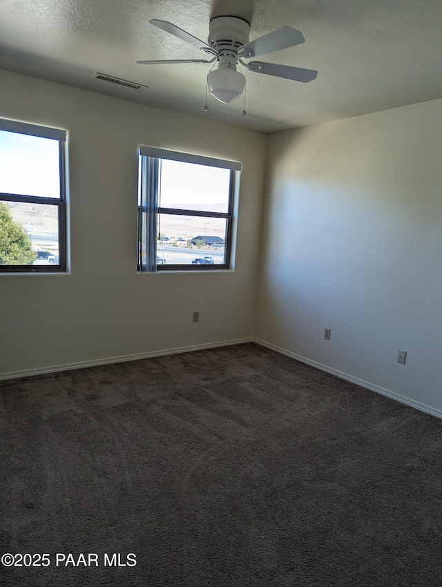 spare room with a textured ceiling, visible vents, baseboards, a ceiling fan, and dark colored carpet