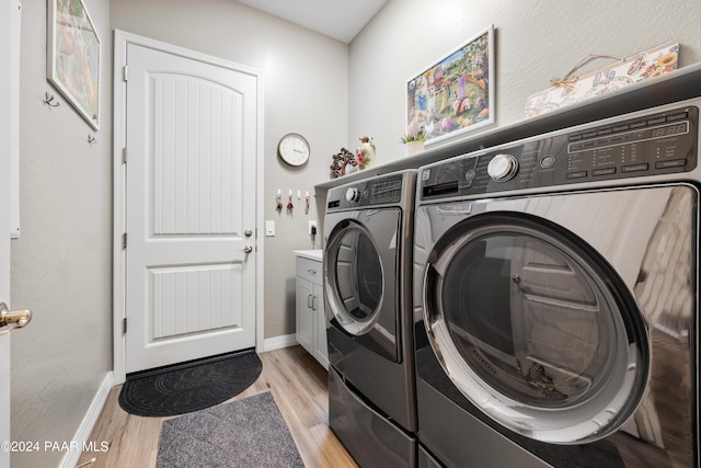 clothes washing area featuring cabinets, light hardwood / wood-style floors, and washer and clothes dryer