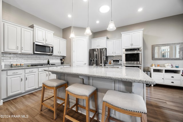 kitchen featuring hardwood / wood-style floors, a center island with sink, hanging light fixtures, white cabinetry, and stainless steel appliances