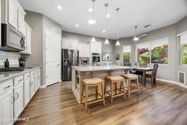 kitchen with backsplash, a center island with sink, white cabinets, and stainless steel appliances