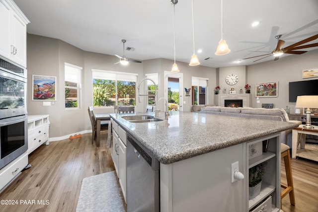 kitchen featuring white cabinetry, an island with sink, decorative light fixtures, appliances with stainless steel finishes, and light wood-type flooring