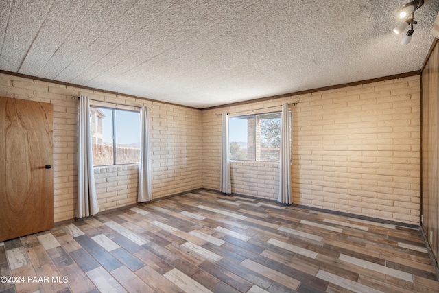 unfurnished bedroom with crown molding, hardwood / wood-style floors, brick wall, and a textured ceiling