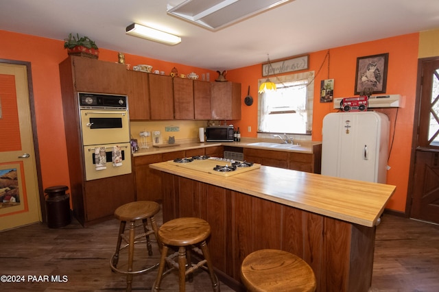 kitchen with white appliances, brown cabinetry, a kitchen breakfast bar, dark wood-style flooring, and a sink