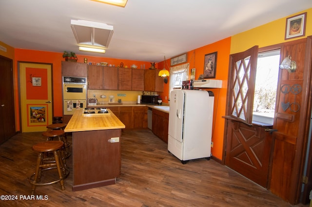 kitchen with brown cabinets, wooden counters, dark wood-type flooring, white appliances, and a kitchen breakfast bar