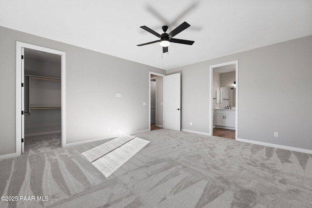 unfurnished bedroom with a ceiling fan, carpet, baseboards, a walk in closet, and connected bathroom