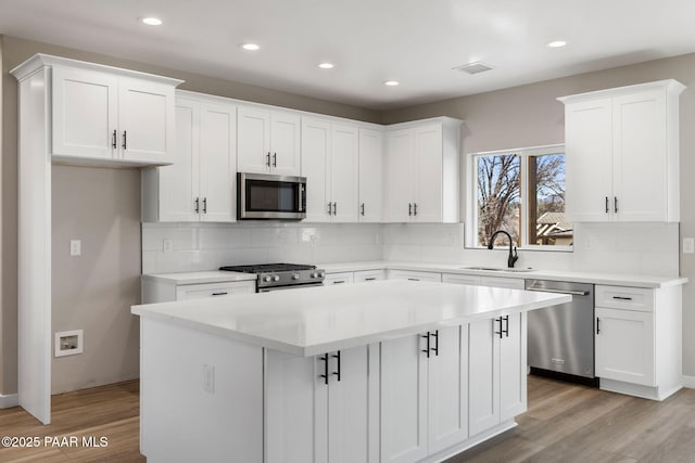 kitchen featuring a sink, a kitchen island, light wood-style floors, appliances with stainless steel finishes, and white cabinets