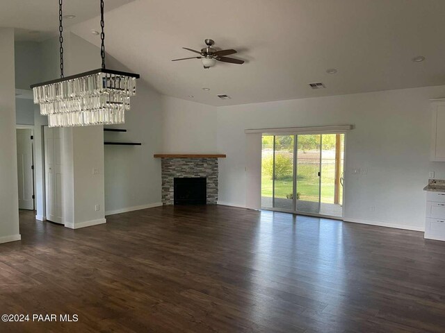 unfurnished living room with a stone fireplace, dark wood-type flooring, and ceiling fan with notable chandelier