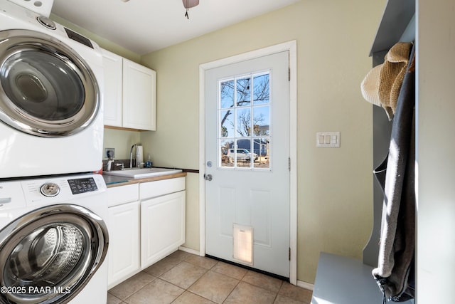 clothes washing area featuring ceiling fan, sink, stacked washer / dryer, light tile patterned floors, and cabinets