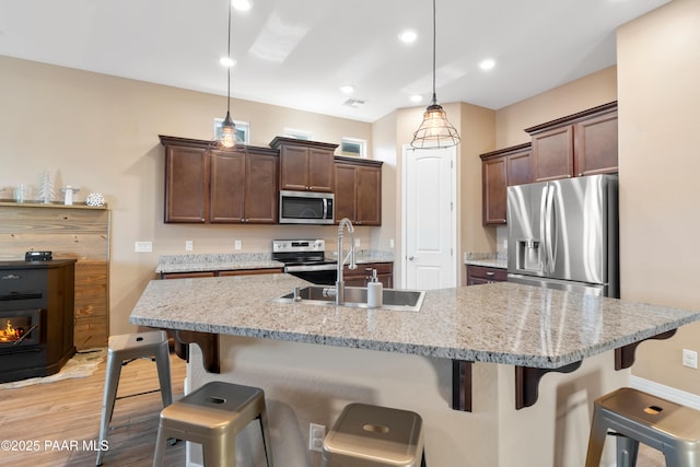 kitchen with sink, stainless steel appliances, decorative light fixtures, a kitchen island with sink, and a breakfast bar