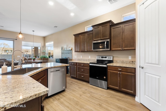 kitchen with sink, hanging light fixtures, light wood-type flooring, dark brown cabinetry, and stainless steel appliances