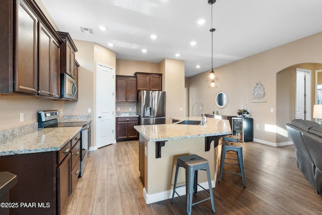 kitchen featuring a breakfast bar, sink, light hardwood / wood-style flooring, decorative light fixtures, and stainless steel appliances