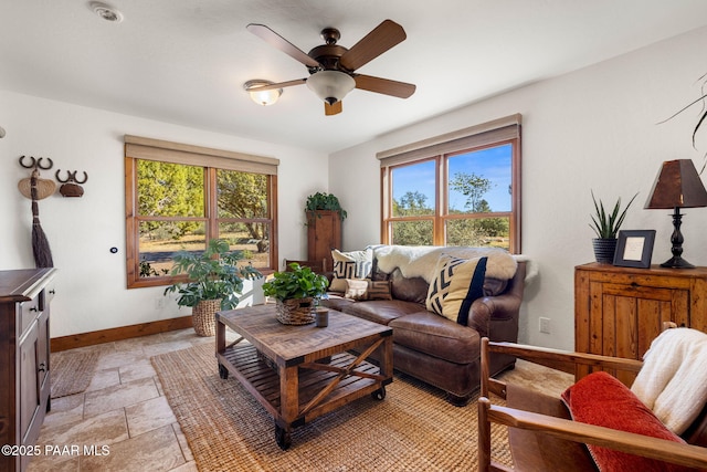 living room featuring stone tile flooring, a ceiling fan, and baseboards