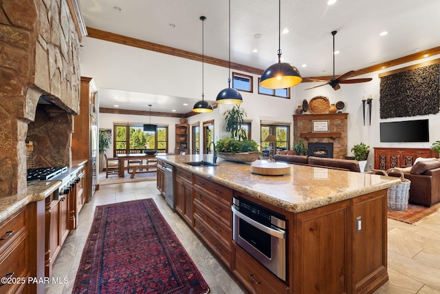 kitchen with a ceiling fan, a fireplace, a sink, appliances with stainless steel finishes, and crown molding