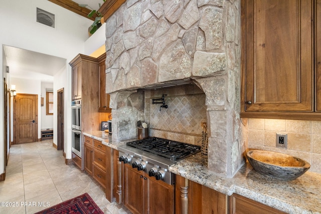 kitchen with brown cabinetry, visible vents, appliances with stainless steel finishes, and light stone countertops