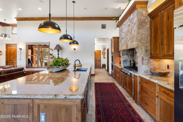 kitchen featuring brown cabinetry, a large island with sink, stainless steel appliances, a sink, and tasteful backsplash