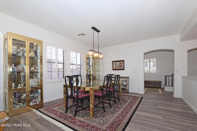 dining room featuring arched walkways, visible vents, wood finished floors, and baseboards