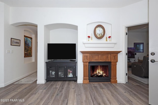 living room with wood finished floors, a warm lit fireplace, and baseboards