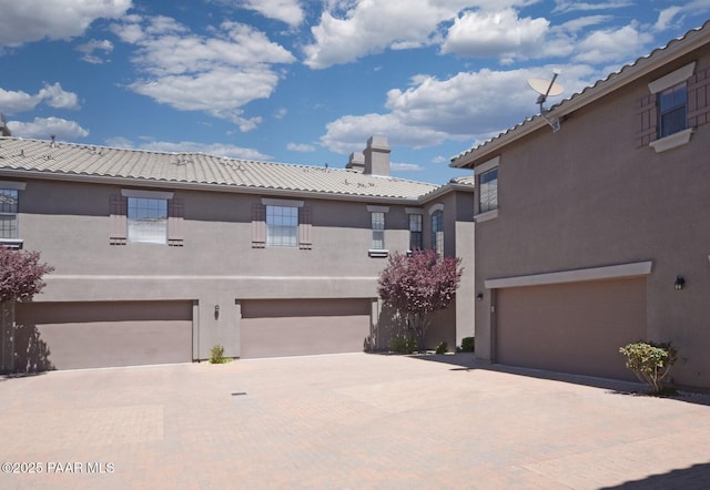exterior space with a chimney, stucco siding, a garage, a tile roof, and driveway