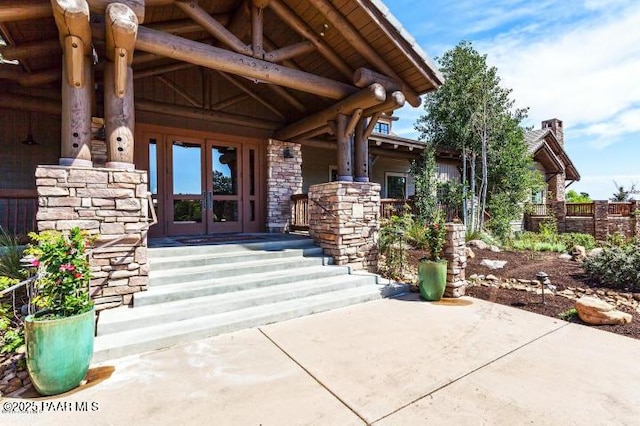 view of exterior entry with covered porch, fence, french doors, and stone siding