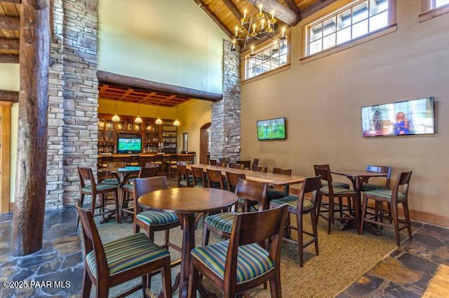 dining area with a notable chandelier, beam ceiling, decorative columns, stone floors, and high vaulted ceiling