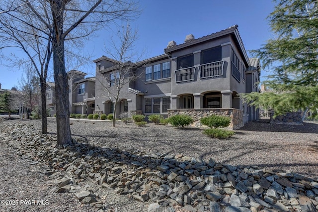 view of front of property featuring a chimney, stone siding, stucco siding, and a balcony