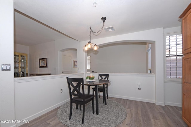 dining area with wood finished floors, visible vents, baseboards, and arched walkways