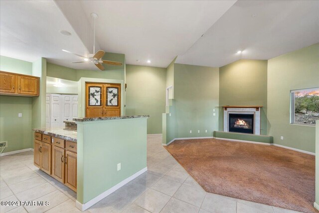 kitchen with ceiling fan, a kitchen island, light tile patterned floors, and stone counters