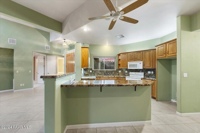 kitchen with ceiling fan, dark stone counters, white appliances, a breakfast bar, and a kitchen island