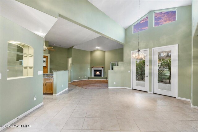 unfurnished living room with light tile patterned floors, ceiling fan with notable chandelier, and high vaulted ceiling