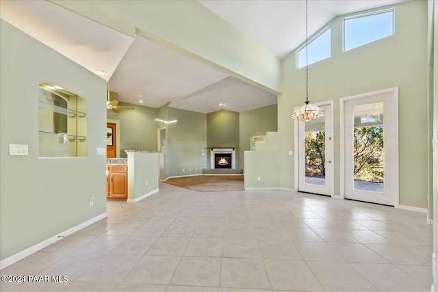 unfurnished living room featuring light tile patterned floors, ceiling fan with notable chandelier, and high vaulted ceiling