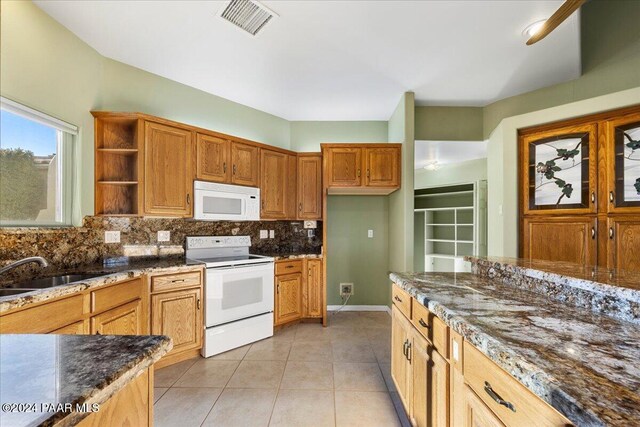 kitchen with sink, tasteful backsplash, dark stone countertops, white appliances, and light tile patterned floors