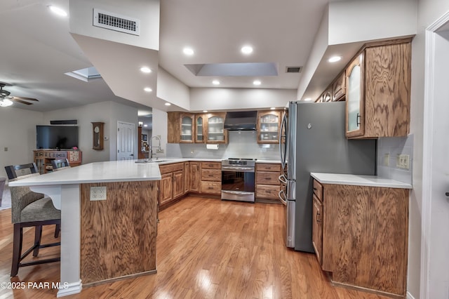 kitchen featuring sink, a kitchen breakfast bar, stainless steel appliances, kitchen peninsula, and wall chimney exhaust hood