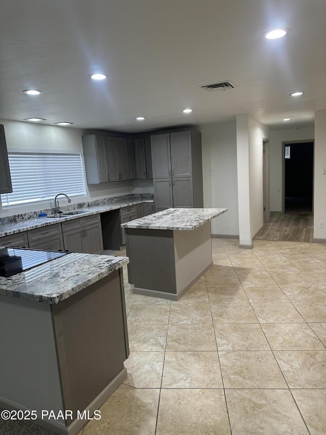 kitchen featuring light stone countertops, a center island, and gray cabinetry