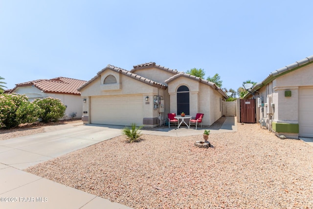 mediterranean / spanish home with stucco siding, an attached garage, a gate, driveway, and a tiled roof