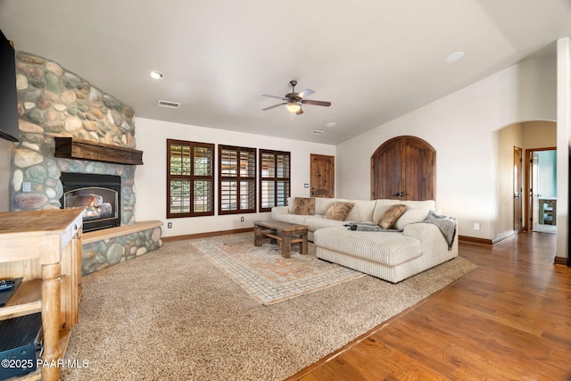 living room featuring wood finished floors, visible vents, a fireplace, arched walkways, and ceiling fan