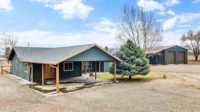 view of front facade featuring gravel driveway, an outdoor structure, a detached garage, and a shingled roof