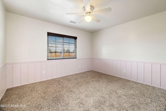 empty room with visible vents, wainscoting, carpet flooring, and ceiling fan