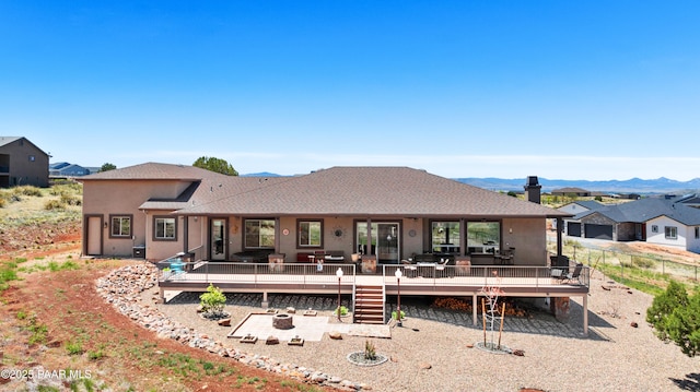 rear view of property featuring a deck with mountain view, fence, and stucco siding